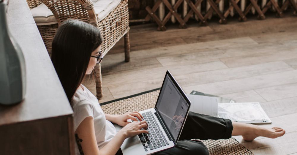 Referral Program - Young barefoot woman using laptop on floor near books in stylish living room