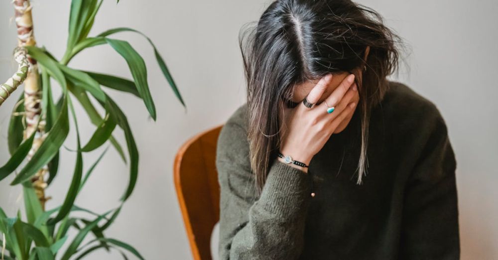 Mistakes - Unrecognizable young upset female millennial with dark hair in stylish sweater covering face with hand while siting on chair at home