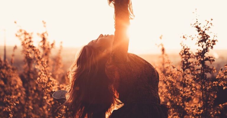 Flexible Hours - Side view of graceful woman leaning back with raised leg while dancing between shrubs in countryside in back lit