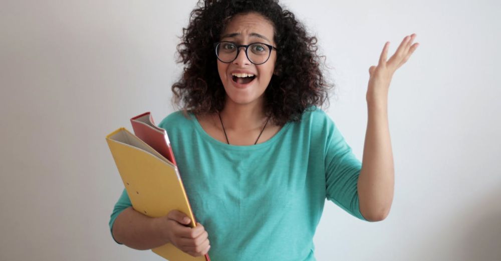 Mistakes - Dissatisfied annoyed woman with mouth opened wearing glasses and turquoise blouse looking away and screaming while standing against white wall with folders of documents and having problems in work